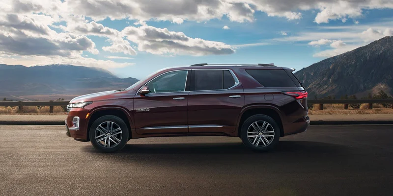 Brand new 2023 Chevrolet Traverse driving along a mountainous highway with valleys and and beautiful blue sky with puffy white clouds in the background.