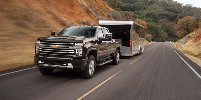 brand new 2023 Chevrolet Silverado 2500 hauling a cargo trailer driving up a beautiful forestry mountainous road.