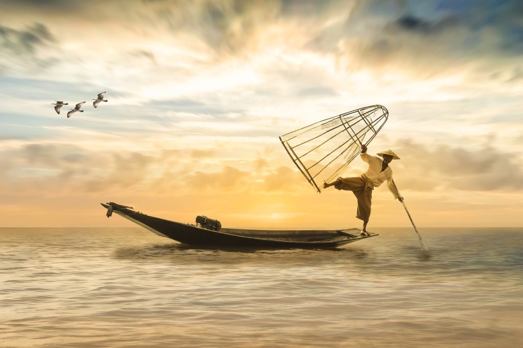 fisherman in the middle of the ocean with a beautiful golden sunset behind him fishing