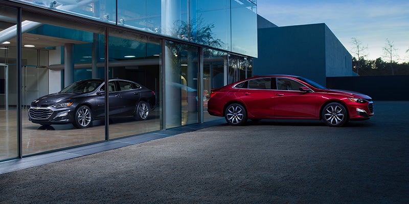 Two brand new Chevrolet Malibu's, one red (outside) and one black (inside the showroom)!